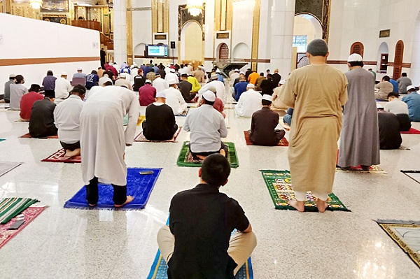 Congregants performing prayers while maintaining physical distance; and a uniformed personnel checks the validity of a congregant’s BruHealth status at a mosque’s entrance. PHOTOS: AZLAN OTHMAN