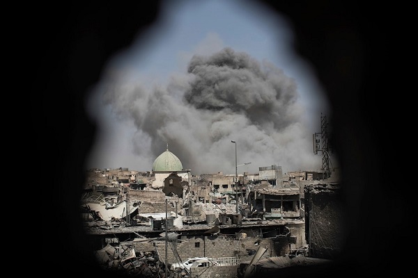 A bomb explodes behind the al-Nuri Mosque complex as seen through a hole in the wall of a house in June 2019
