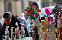 یک زن مصری در بازاری در قاهره، در حال نگاه کردن به قیمت شیرینی‌های سنتی و «عروسه المولد» (عروسک‌های مخصوص جشن میلاد) است.