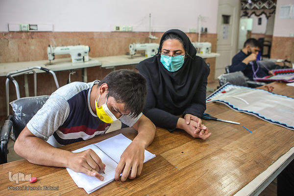خانم مرادی استاد کارگاه صنایع دستی در حال آموزش خواندن و نوشتن به یکی از توانیابان است.