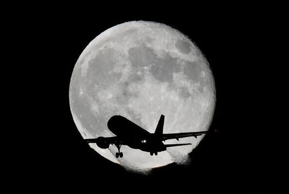 یک هواپیما هنگام فرود به فرودگاه هیترو لندن در بریتانیا از مقابل ماه عبور می کند.