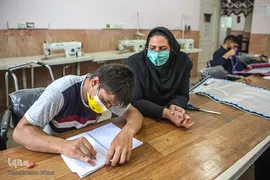 خانم مرادی استاد کارگاه صنایع دستی در حال آموزش خواندن و نوشتن به یکی از توانیابان است.